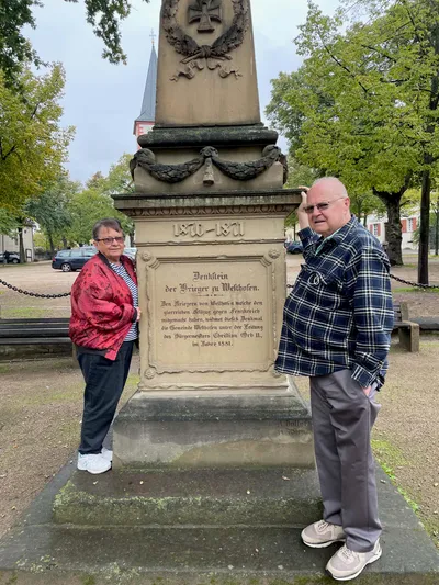 George and his wife with a monument in the hometown of his ancestors.